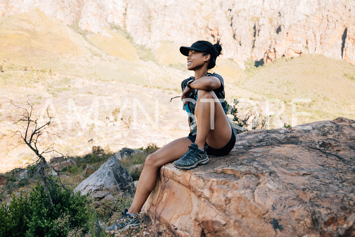 Smiling woman hiker sitting on big stone in valley enjoying the view