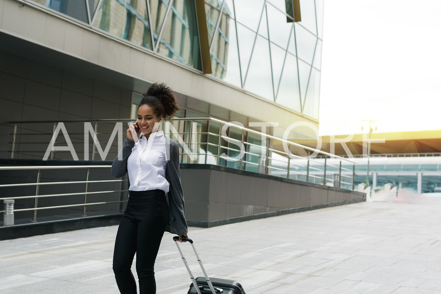 Young woman with luggage walking at terminal, using mobile phone	