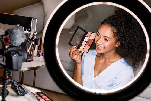 Young smiling woman showing a makeup palette on camera while recording video for beauty channel