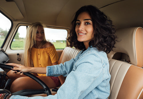 Smiling woman looking outside the car window while driving a van. Women friends enjoying on a road trip.