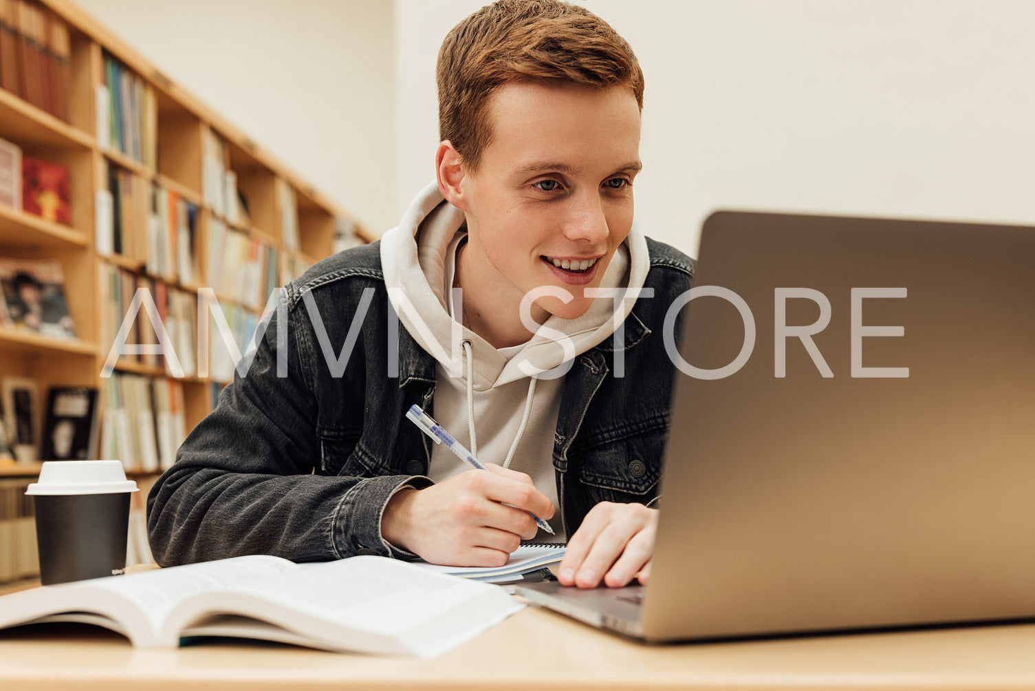 Smiling guy looking at laptop screen while sitting in library