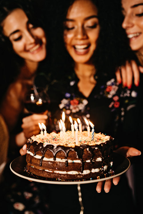 Young woman holding her birthday cake surrounded by friends, selective focus