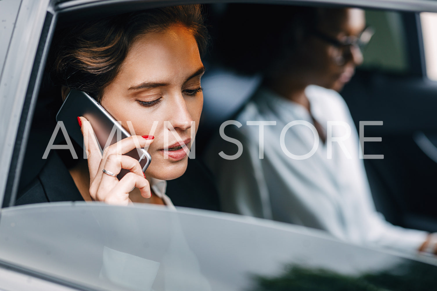 Businesswoman talking on a cell phone while sitting by a female colleague in a taxi	