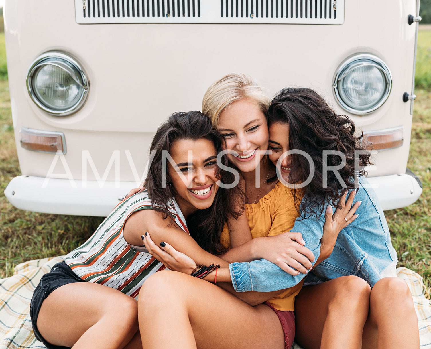 Three happy women embracing each other sitting in front of a minivan during a vacation