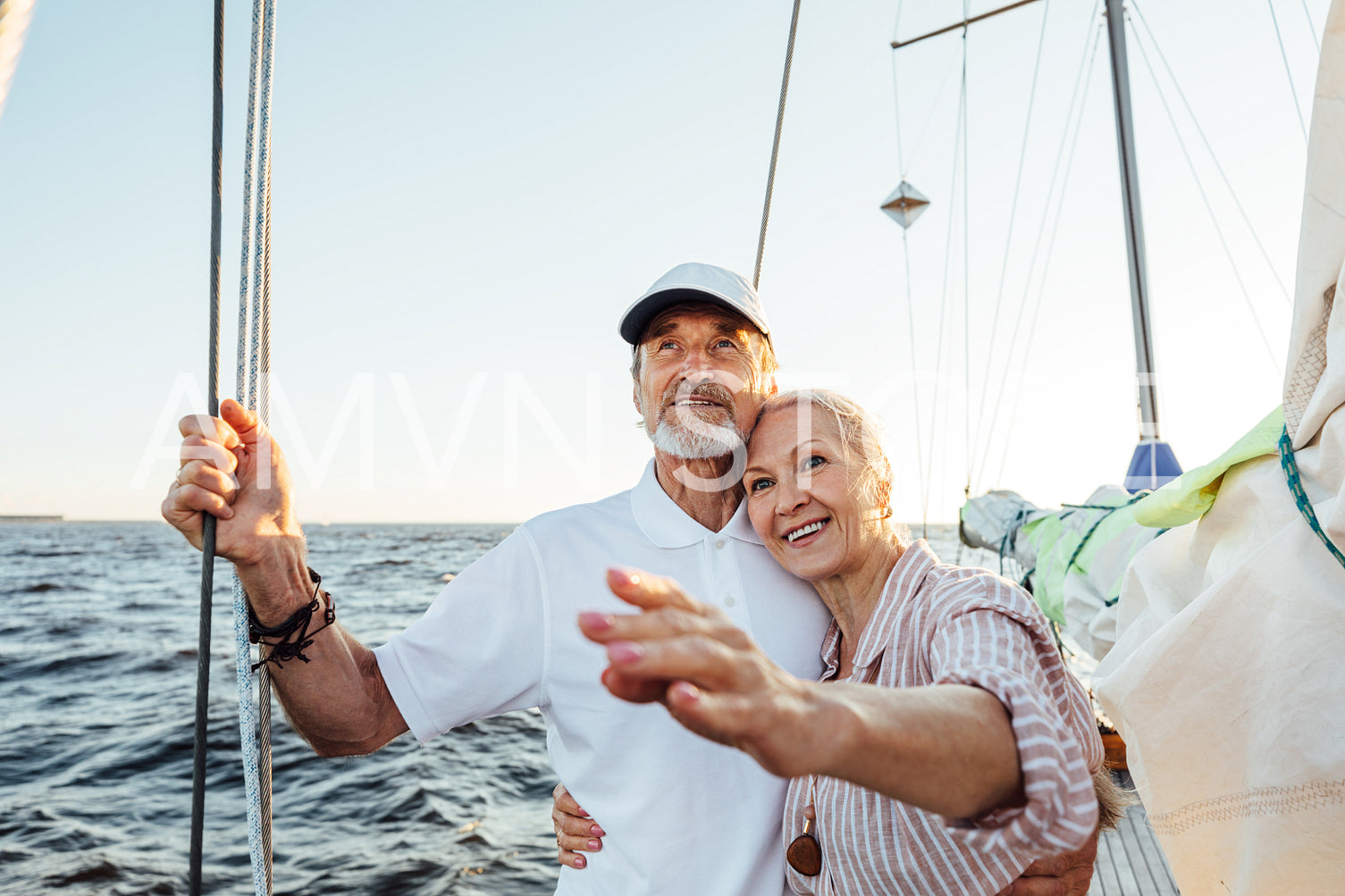 Happy mature woman pointing into the distance while embracing by his husband on their yacht	