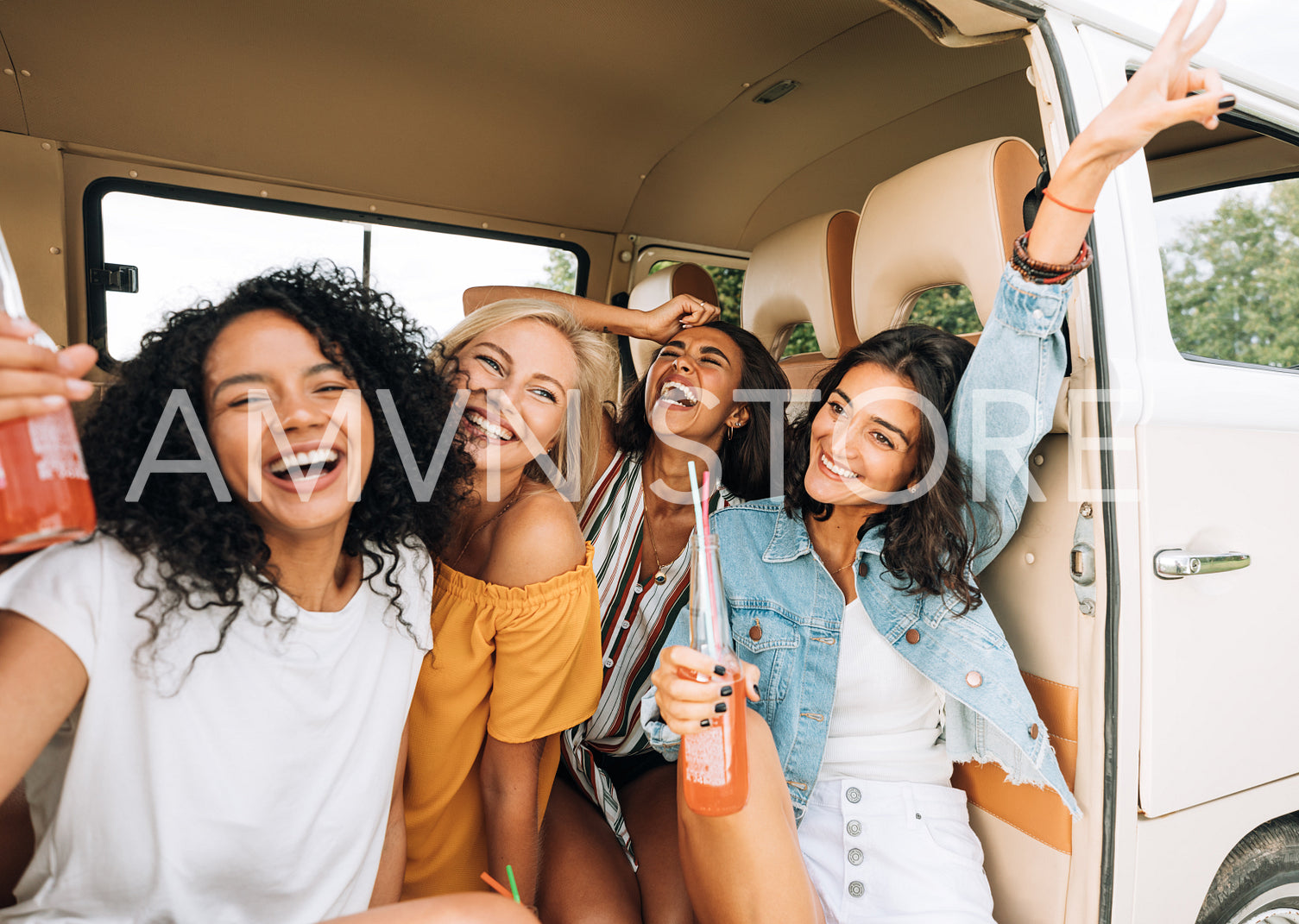 Four cheerful women enjoying holidays sitting in camper van holding cocktails