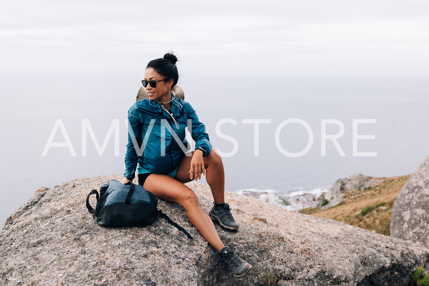 Smiling woman in sports clothes with backpack sitting on a cliff and enjoying the view