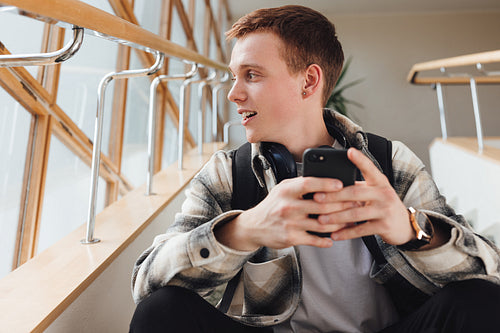 Student sitting on a stairs in college holding smartphone looking at window