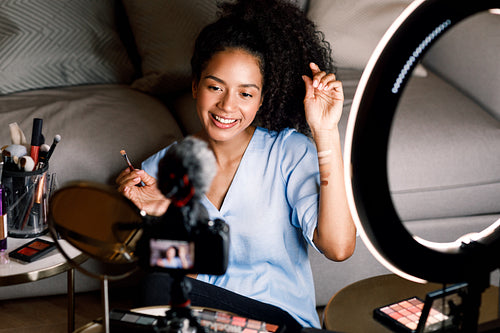 Smiling beauty blogger recording video on DSLR camera from home