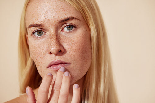 Close up of a woman with freckles touching her lip with a finger. Young blond female applying balm on her lips.