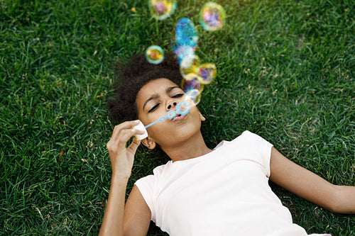 Girl lying on grass blowing bubbles in the air