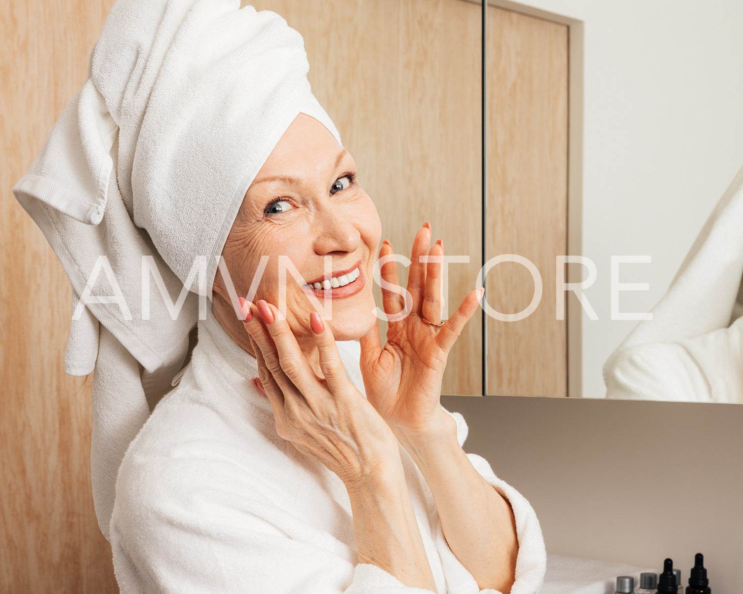 Smiling senior woman with a towel on her head massaging her face and looking at camera