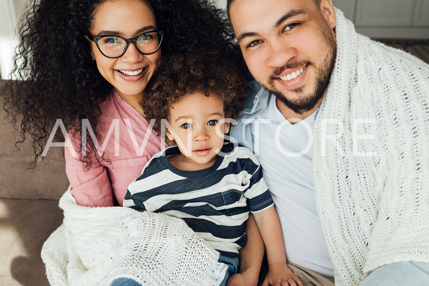 Family of three looking at camera. Mother, father, and son sitting on a couch.	