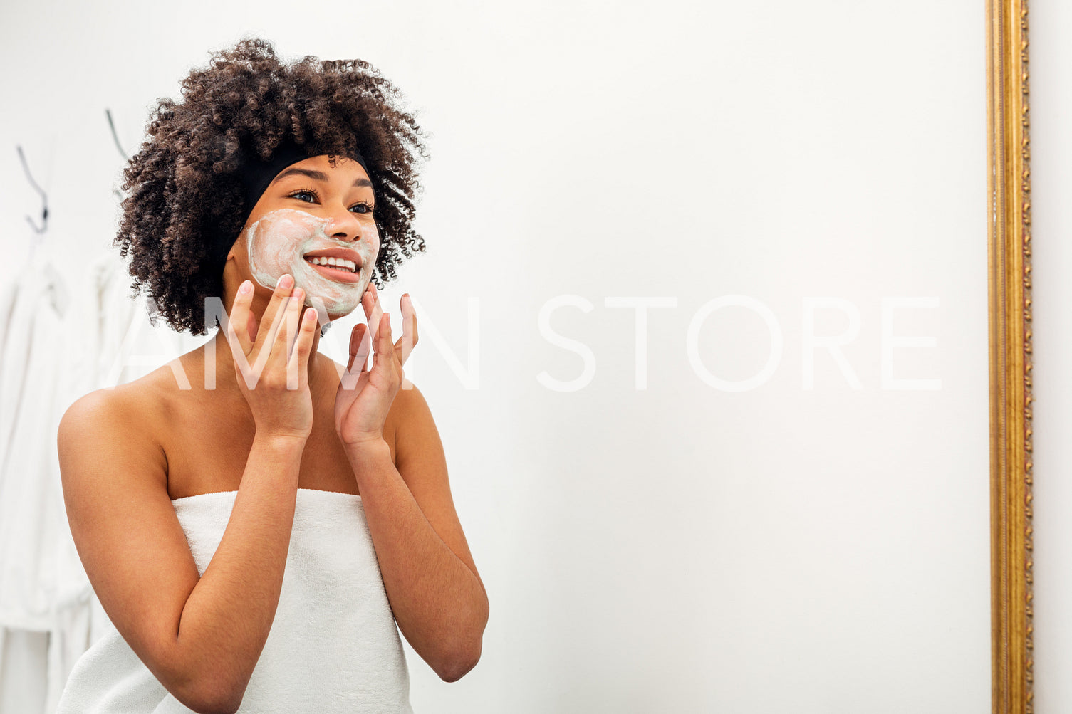 Smiling girl in front of a mirror. Young woman applying white natural mask with hands.	