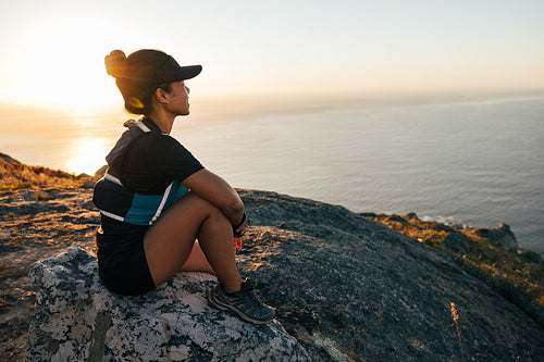 Woman in sportswear enjoying the sunset. Female hiker sitting on rock and looking into a distance.