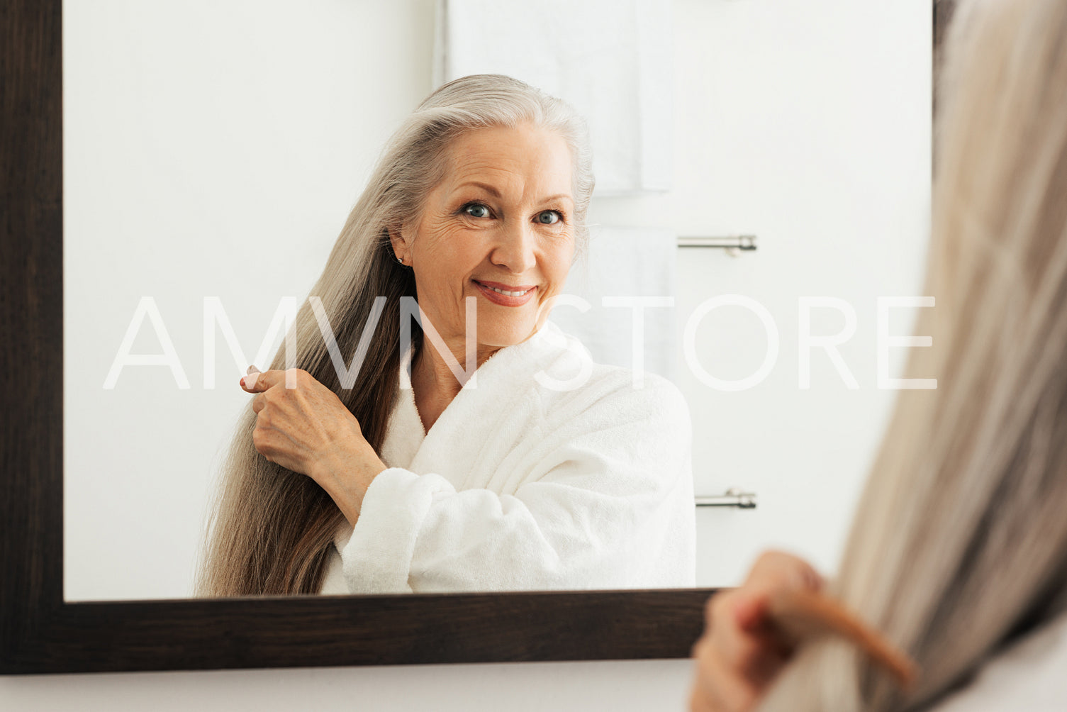 Mature woman combing her long gray hair in front of a mirror