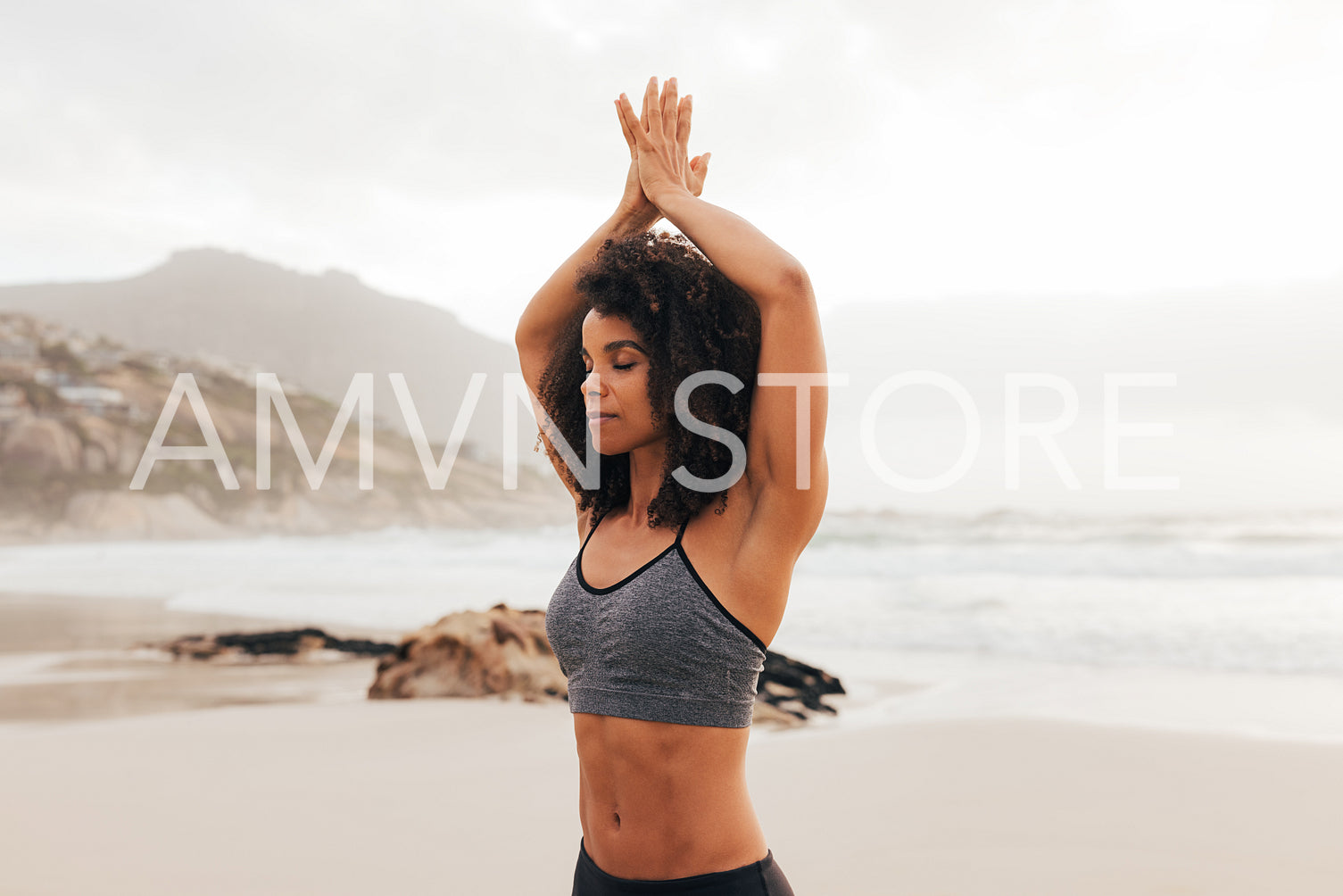 Woman meditating on a beach with closed eyes with hands overhead