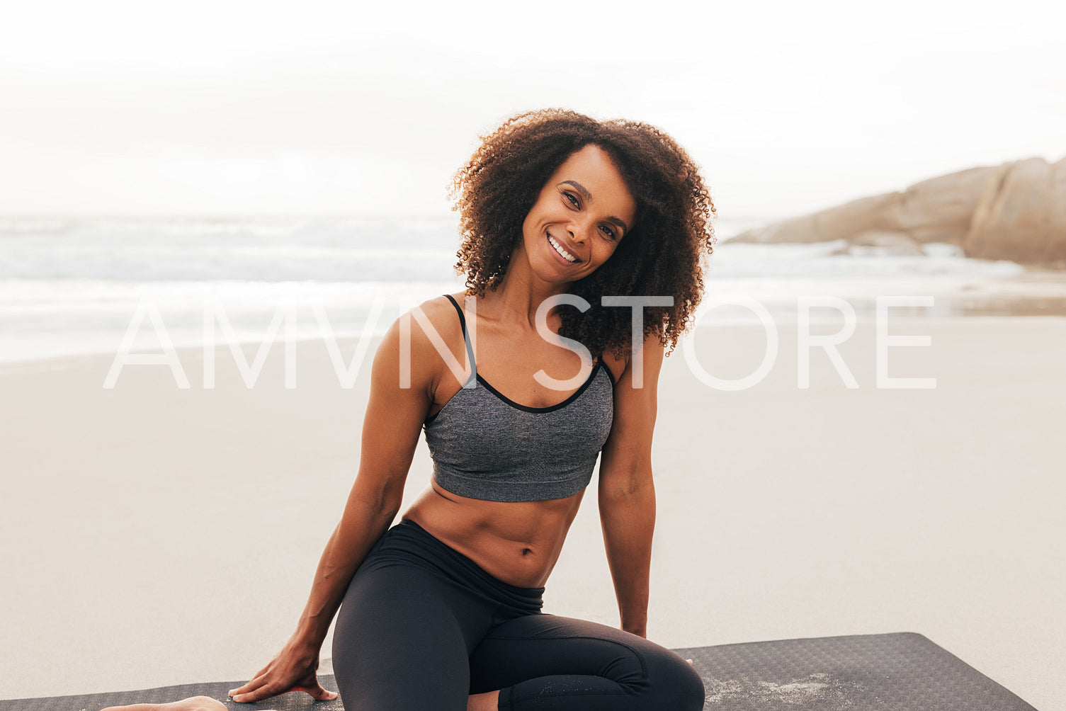 Portrait of a smiling beautiful woman looking at camera while sitting on mat at sunset