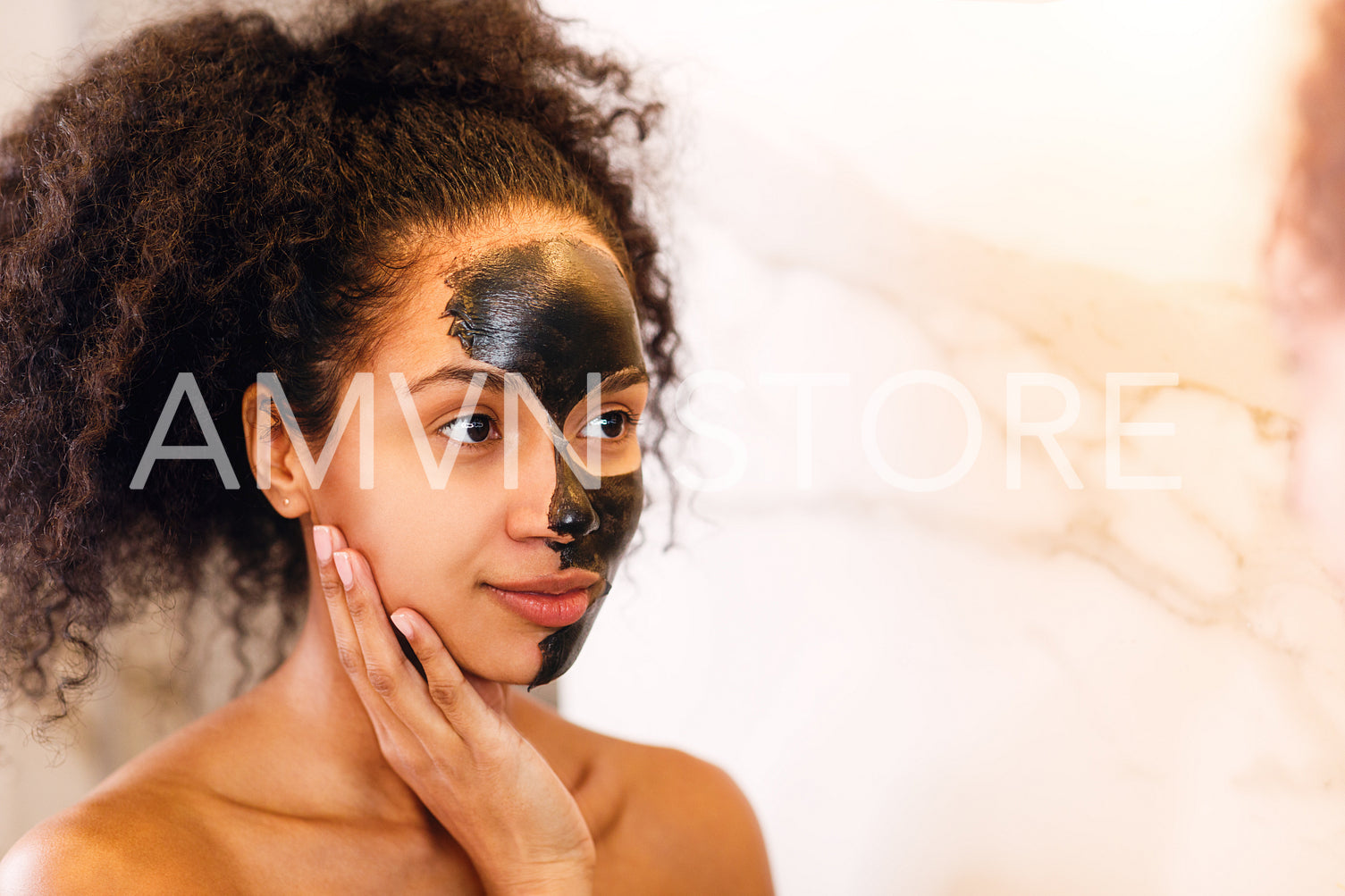 Portrait of beautiful brunette woman with black clay face mask looking at mirror	