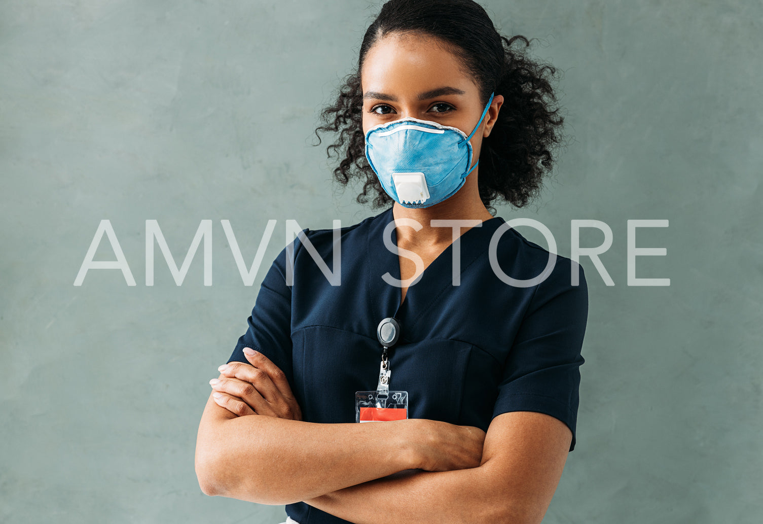 Young nurse in medical uniform with badge standing at wall with crossed arms	