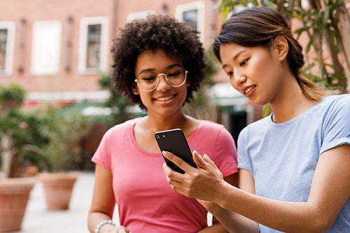 Two female friends looking at smartphone and talking