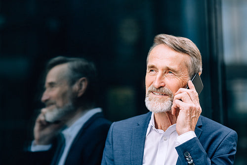 Senior businessman standing outdoors at office building and talking on cell phone