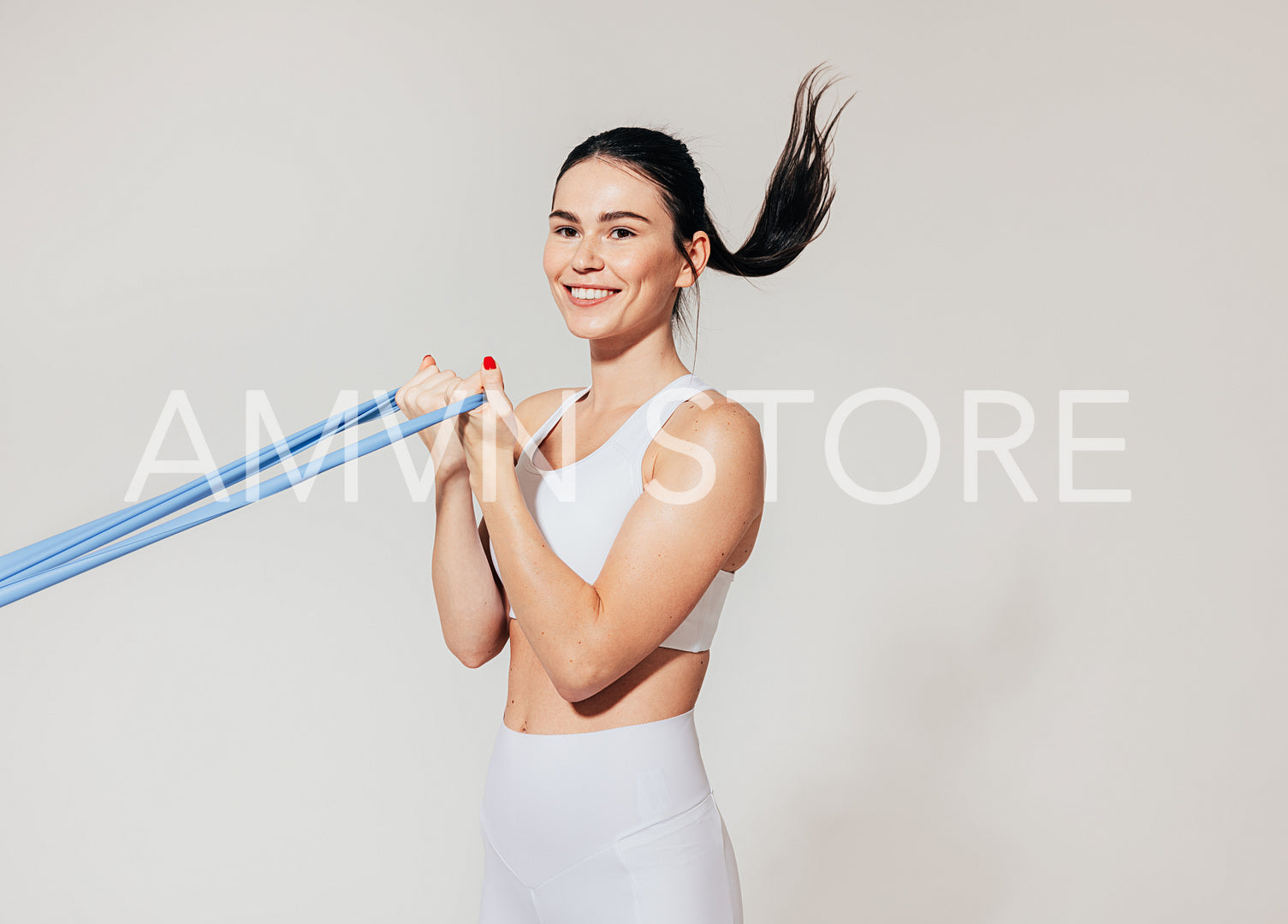 Smiling woman doing biceps curl with resistance band at white wall