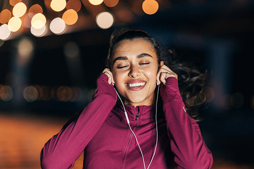 Cheerful woman with closed eyes listening to music during training at night