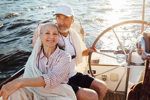 Smiling mature woman looking at camera while her husband steering a sailboat. Two senior people enjoying a vacation on yacht.