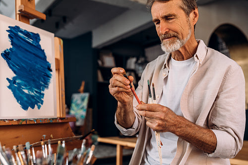 Mature painter checking brush in his studio