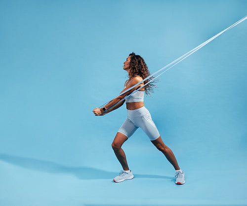 Female working out with elastic band on blue background. Slim athletic woman working on core strength with resistance band.