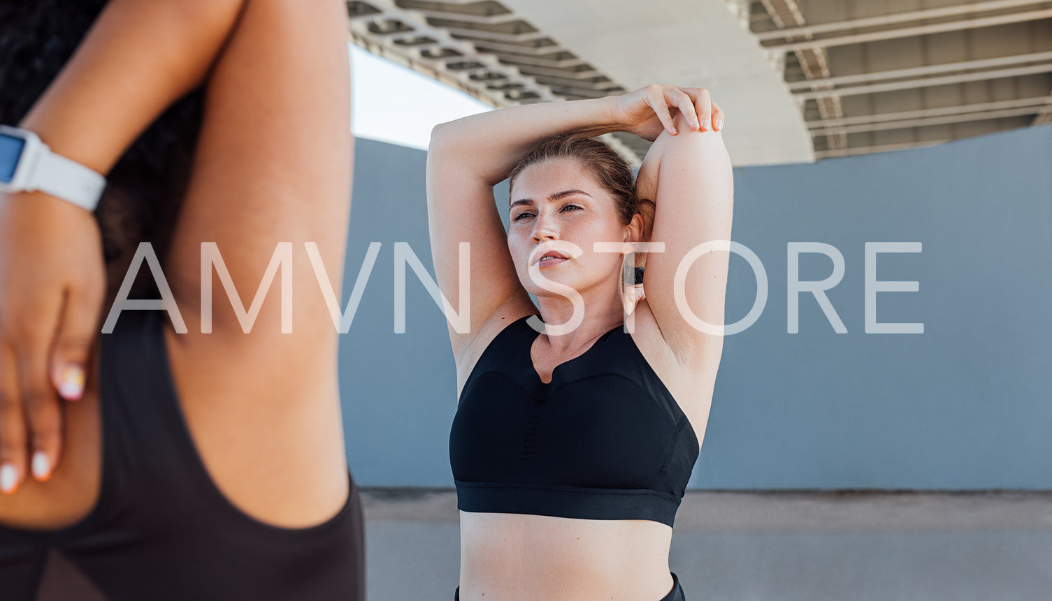 Portrait of a young woman stretching her hand with a fitness buddy. Two fitness females are exercising under bridge.