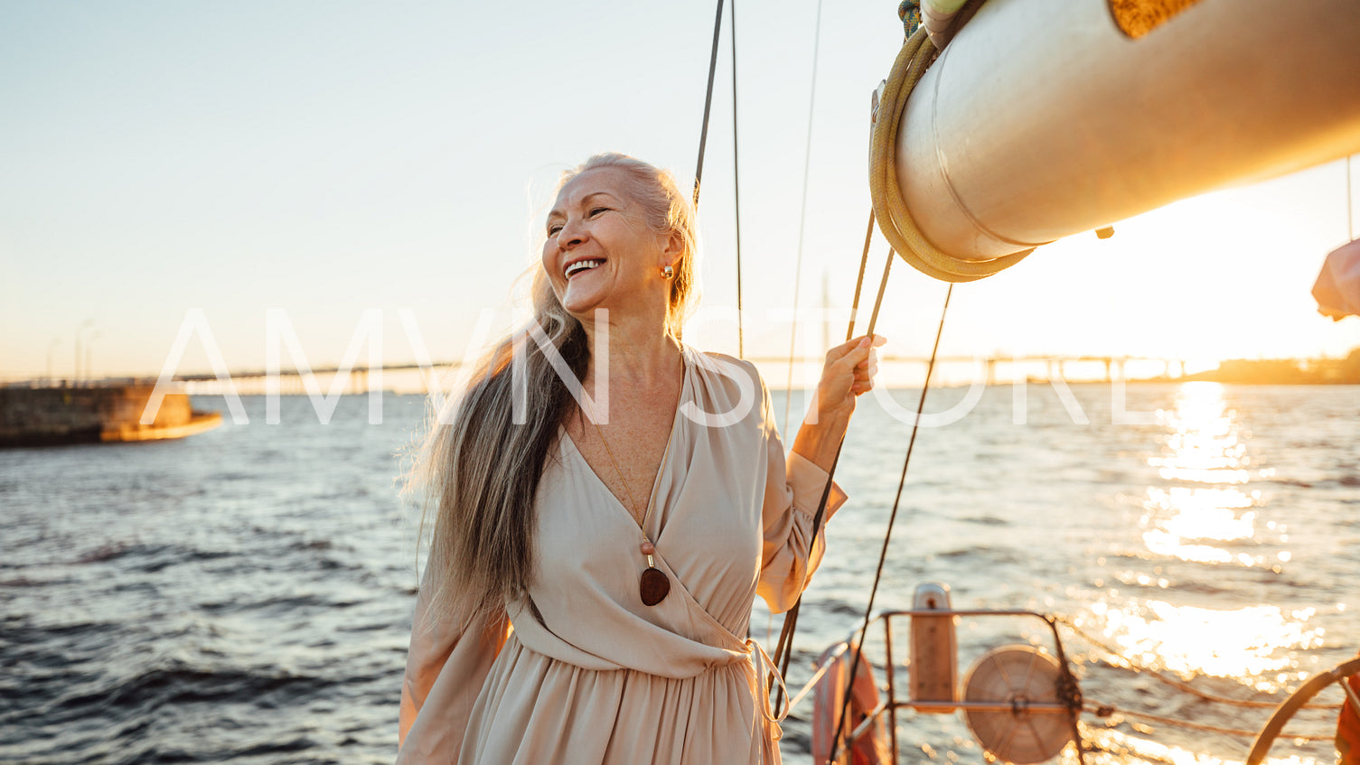 Happy mature woman standing on a yacht at sunset and looking away	