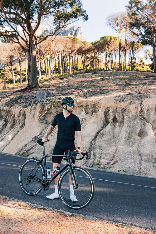 Male cyclist on a roadside with his bicycle. Professional triathlete relaxing.