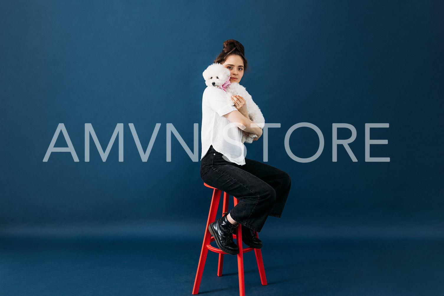 Young female in casuals sitting on a red chair in a studio with her little adorable dog