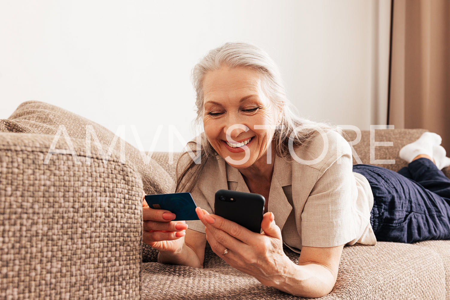 Close up of a senior female holding a credit card and smartphone. Adult smiling woman making a purchase with smartphone at home.