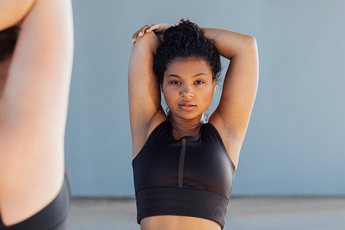 Young woman in black sportswear with curly hair warming up her hand and looking at camera