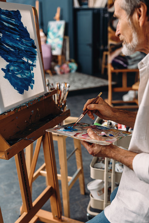 Senior artist working in studio. Painter holding a palette and drawing on canvas.