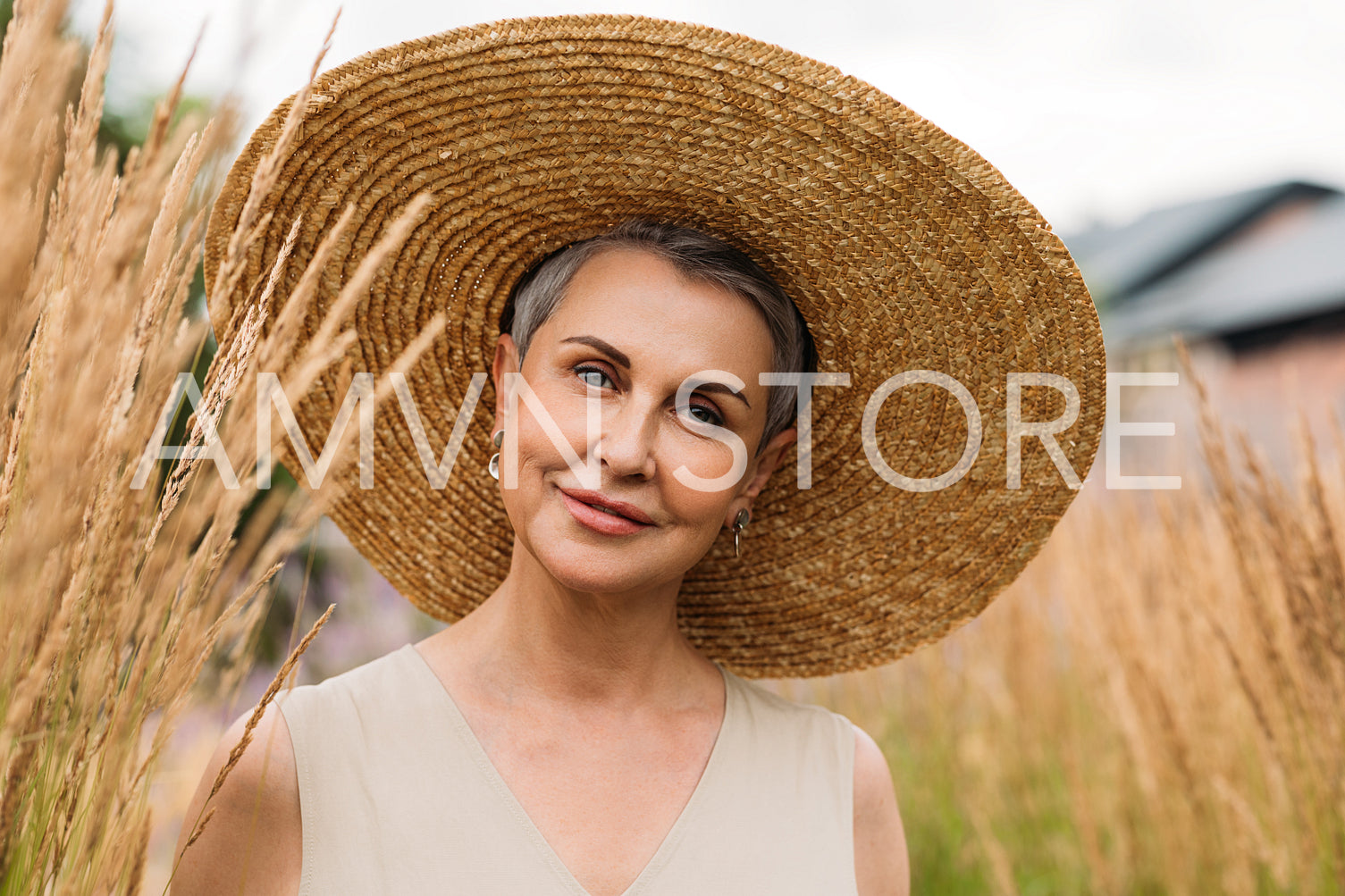 Portrait of an aged woman in a straw hat looking at the camera while standing on the field