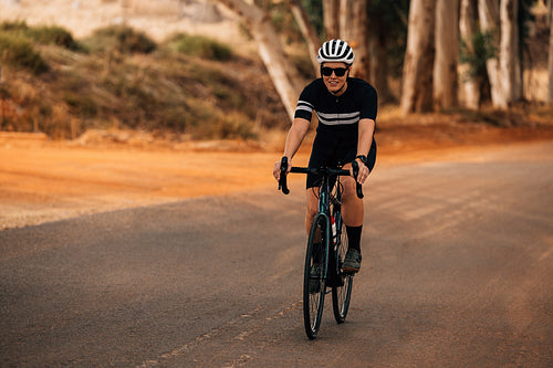 Woman cyclist wearing helmet and sunglasses riding outside on countryside road