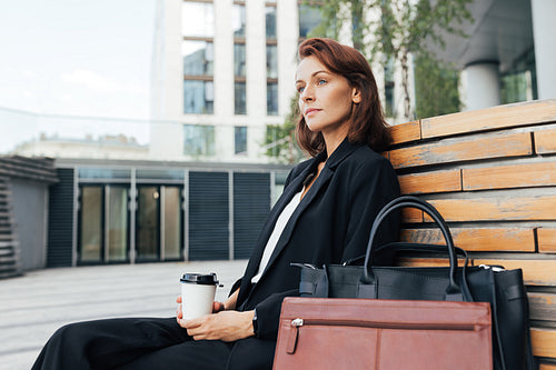 Side view of middle-aged businesswoman sitting outdoors holding a coffee