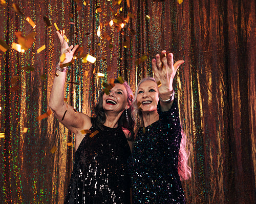 Two smiling senior women in black dresses throwing colorful conf