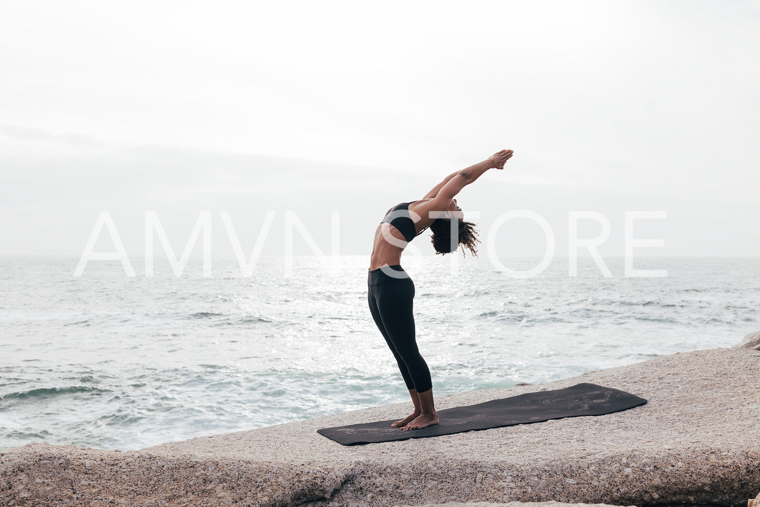 Woman in Standing Backbend Pose by ocean 