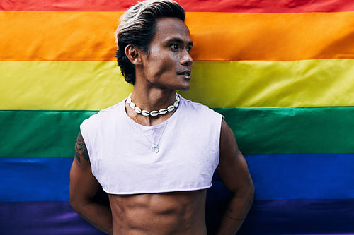 Portrait of a handsome guy looking away while standing against rainbow LGBT flag