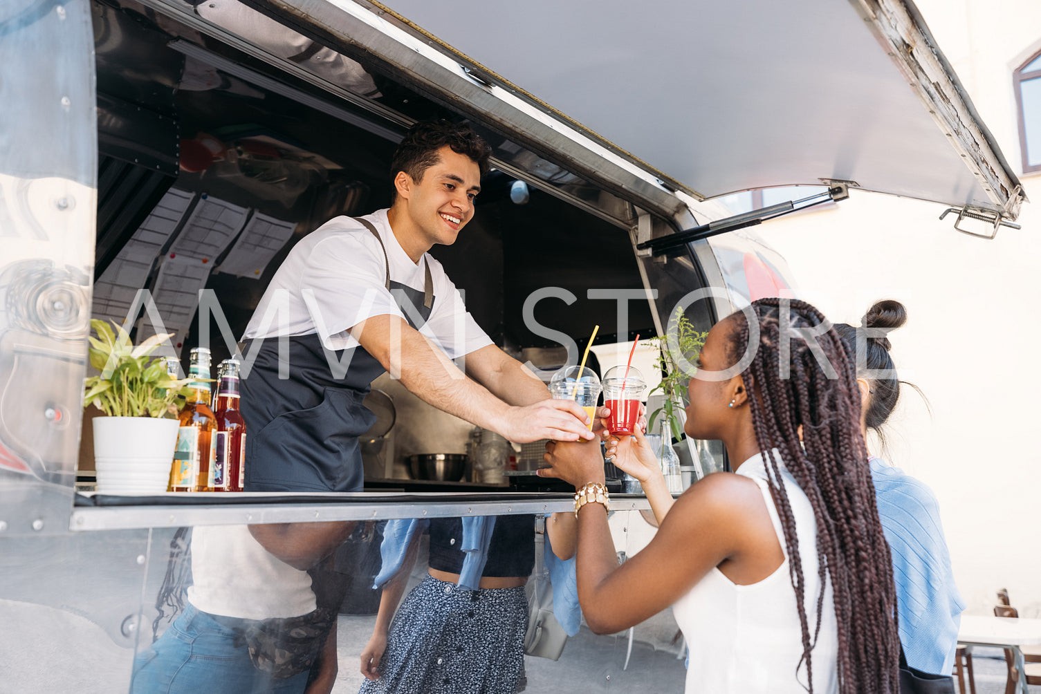 Two customers receiving drinks from food truck owner. Cheerful salesman in apron looking at clients.