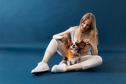 Smiling woman sitting on blue background and playing with her do