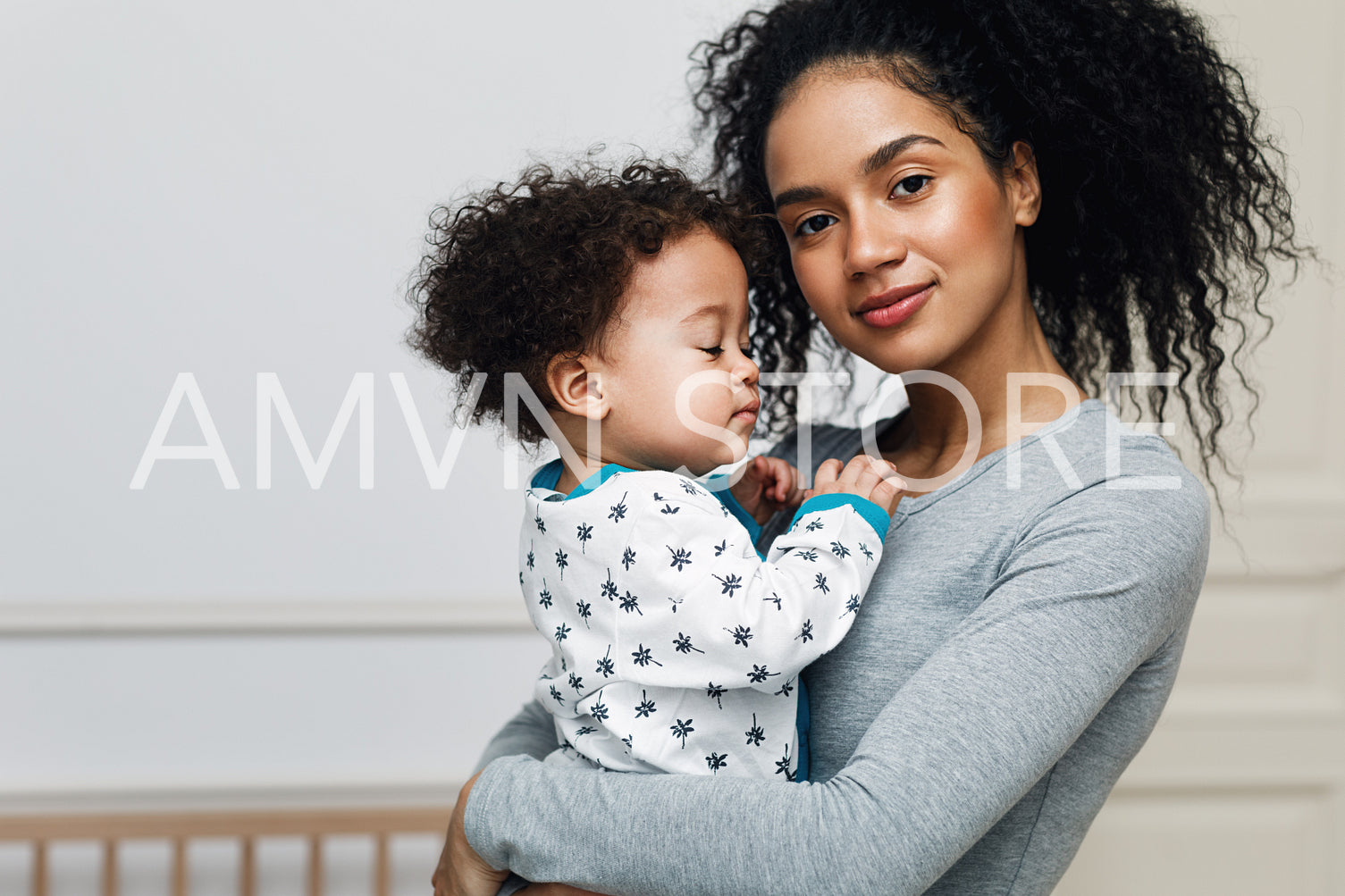 Young mom holding her sleepy baby boy. Beautiful mother with son in living room.	