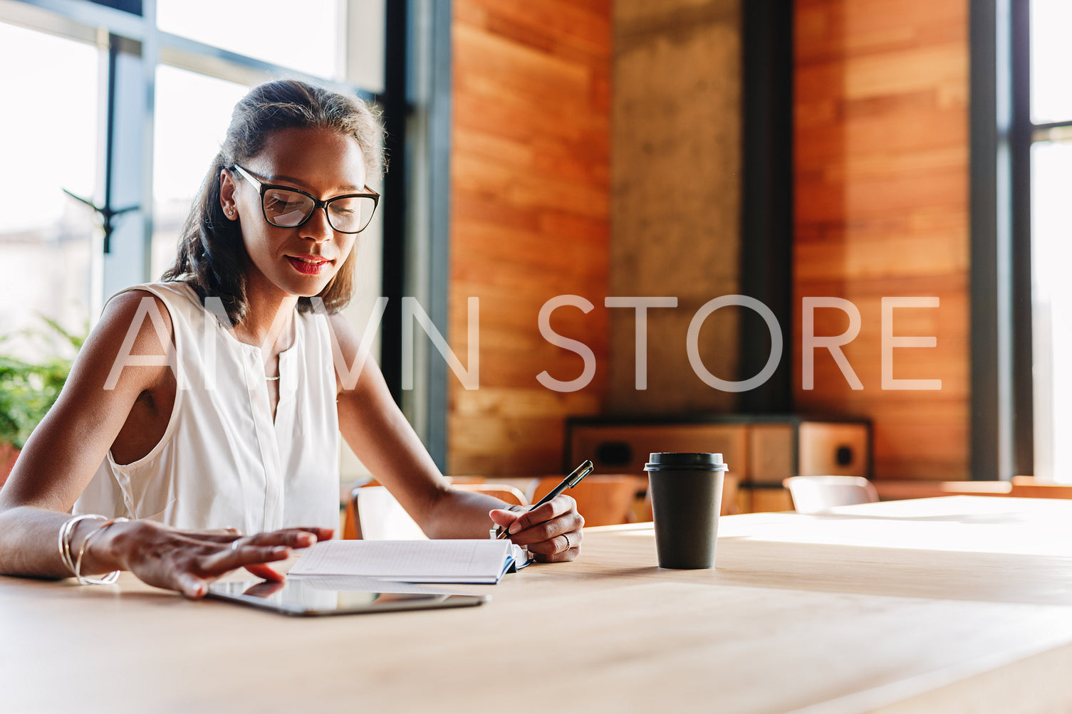 Woman at table browsing digital tablet while taking notes	