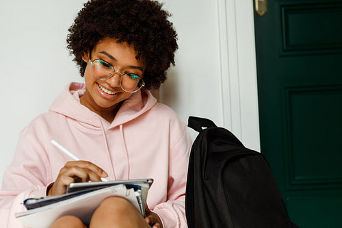 Female student sitting on a floor in campus and writing on digital tablet with stylus