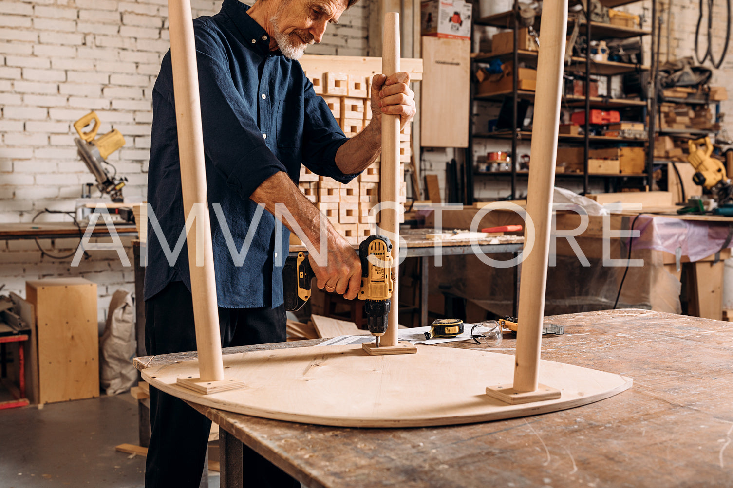 Senior male carpenter drilling a hole in wooden table standing at workbench	